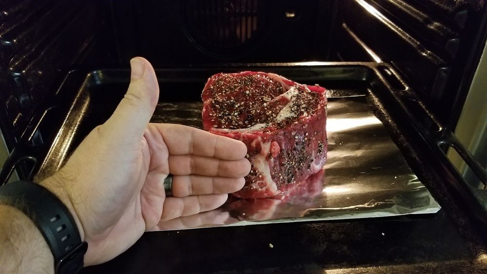 A tray with a thick seasoned raw steak sliding into a hot oven