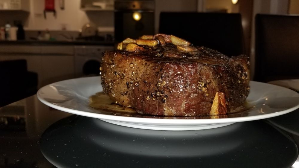 Two thick tied fillet steaks on a wooden board with a plate of diced beef behind